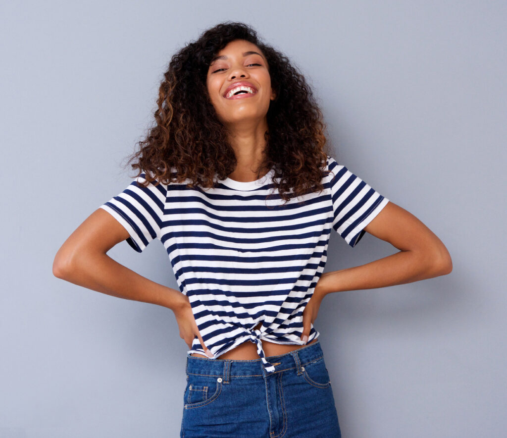 An attractive young black woman smiling against gray background after her dental treatment at Clearly Dental Camden