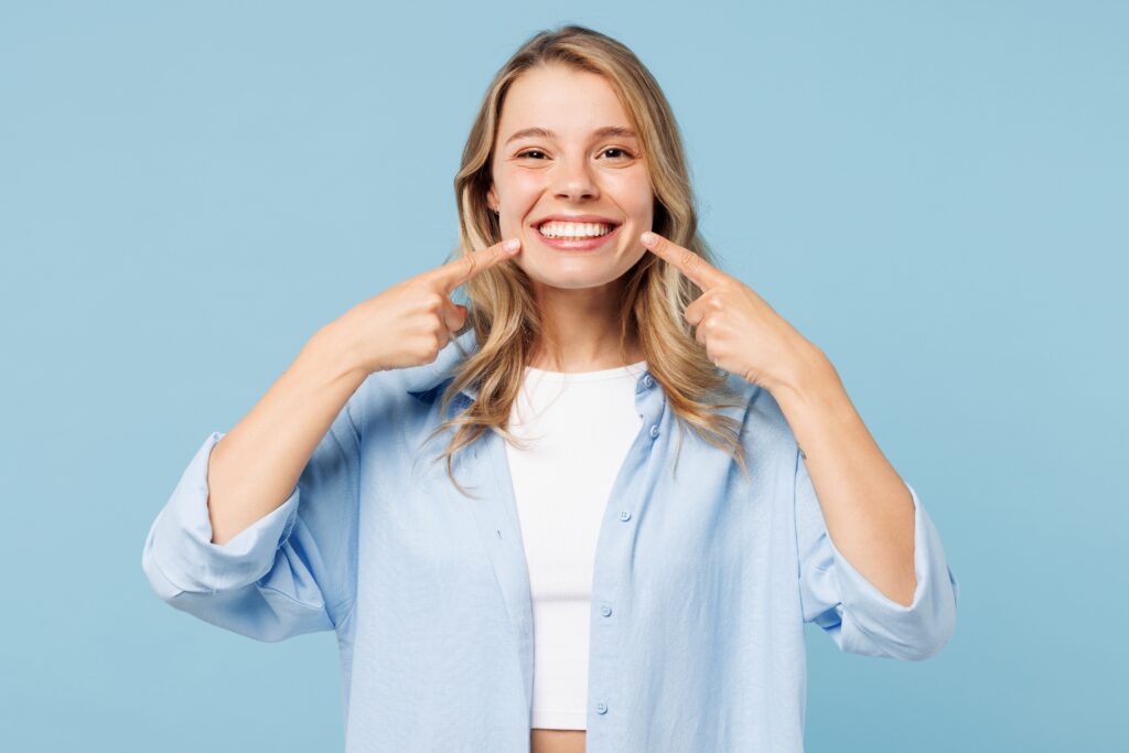 Young woman with long blonde hair smiles and points to her teeth after treatment at Clearly Dental Camden