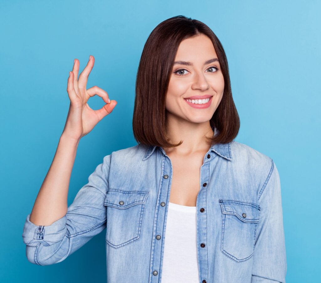Photo of a cheerful woman smiling confidently and showing OK sign after dental care at Clearly Dental Camden