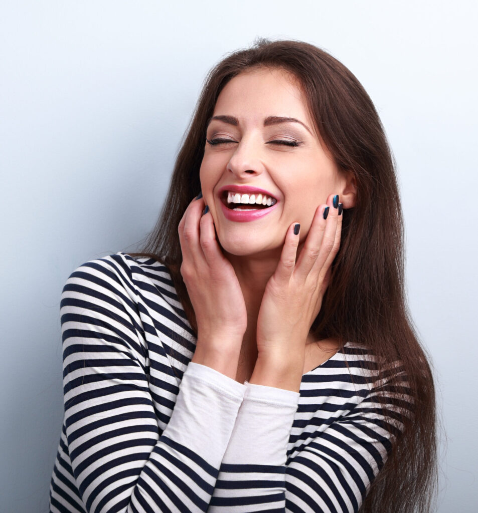 A joyful woman laughs loudly, covering her face after dental treatment at Clearly Dental Camden