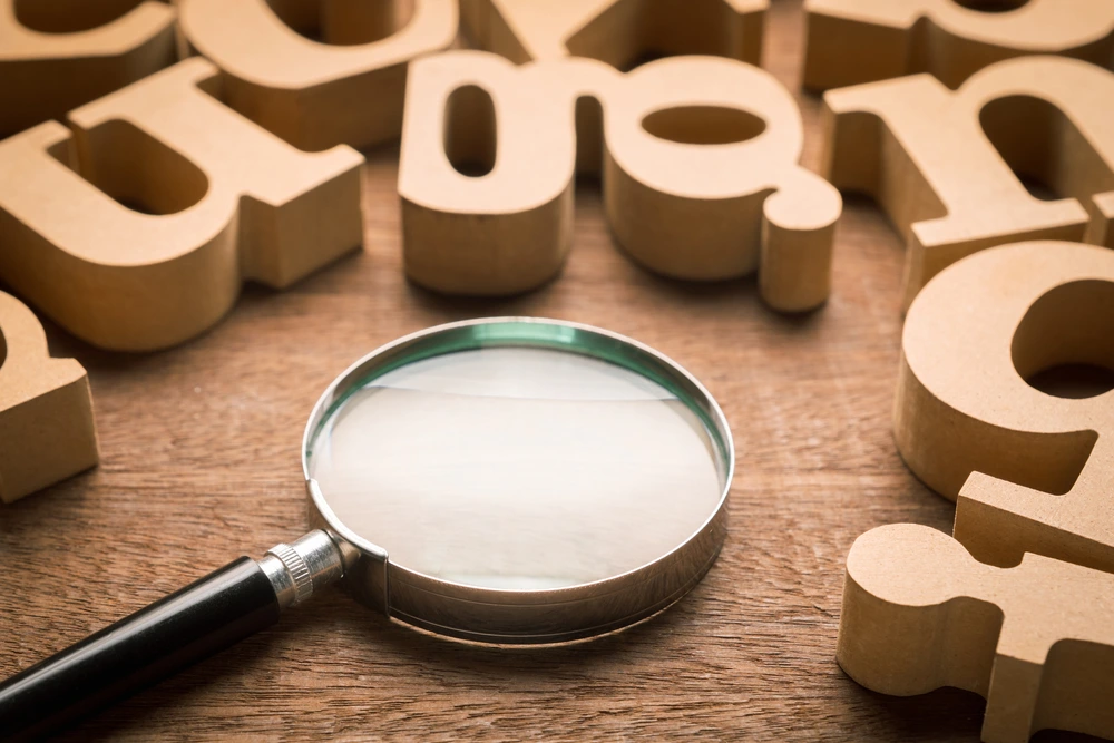 Magnifying glass on wood table with many thick wood English alphabets - Glossary concept of Clearly Dental Camden